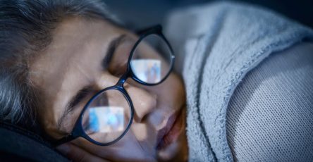 Woman sleeping with television screen reflection in glasses at night