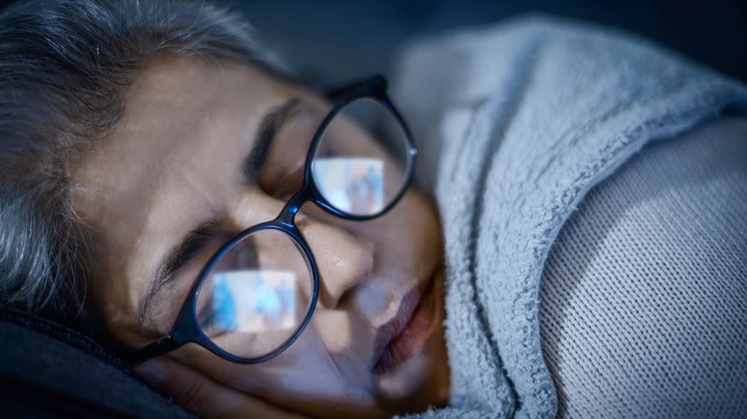 Woman sleeping with television screen reflection in glasses at night